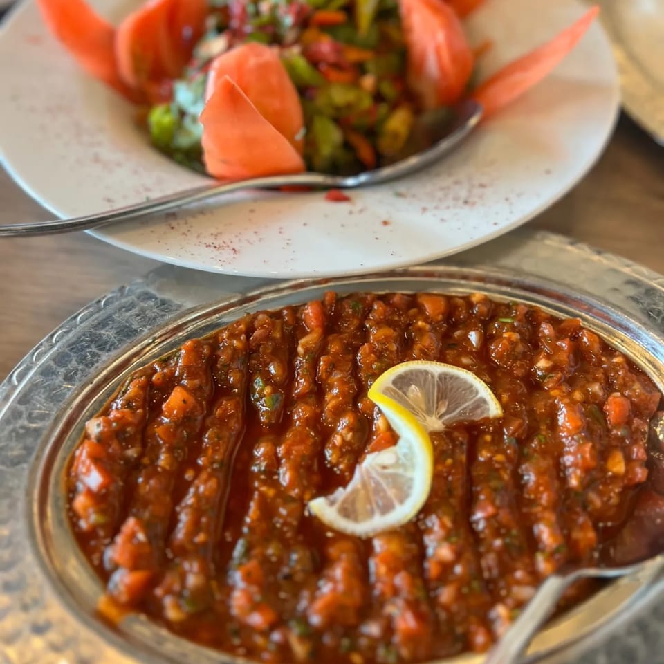 Two Turkish dishes, one a red tomato-based mezze with lemon, the other a green salad.