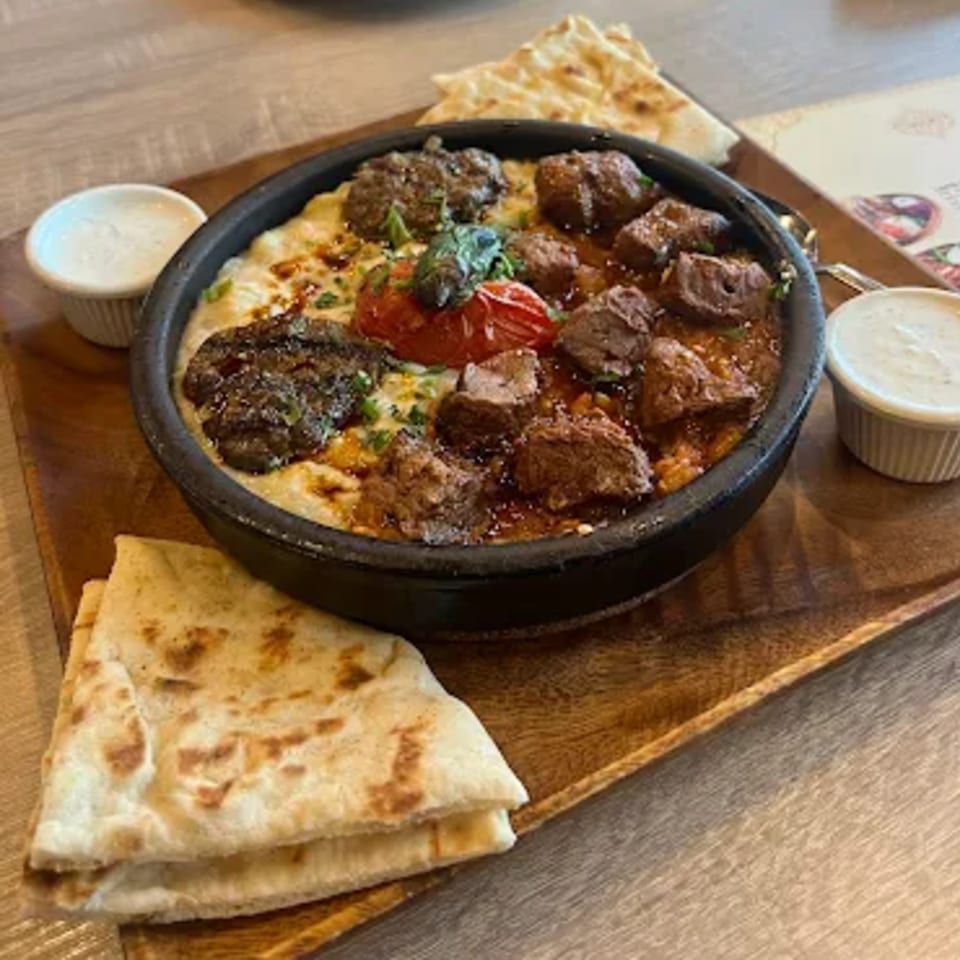 Turkish stew with meat, tomatoes, and herbs in a black bowl, served with flatbread and sauces.