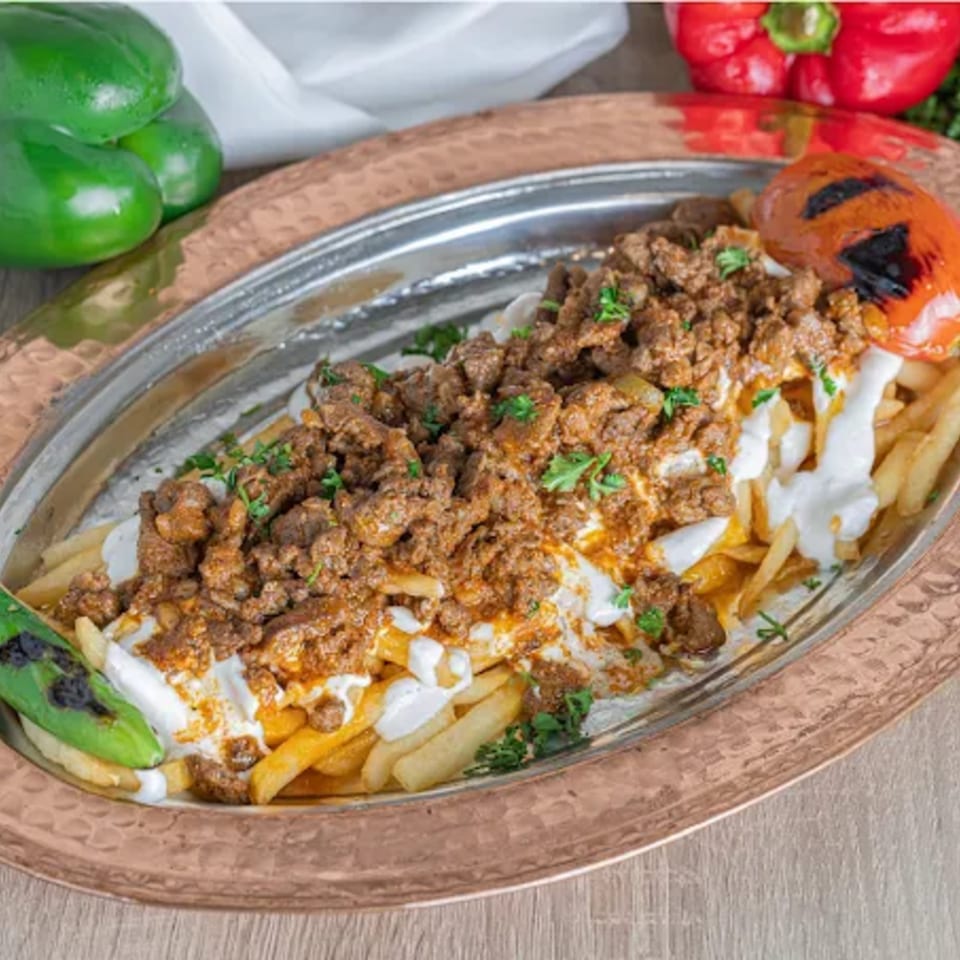 Turkish dish with seasoned ground meat, yogurt sauce, and french fries on a copper platter.