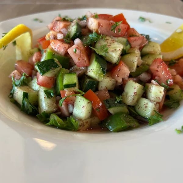 A close-up of a Turkish salad with diced tomatoes, cucumbers, onions, and parsley, garnished with lemon wedges.
