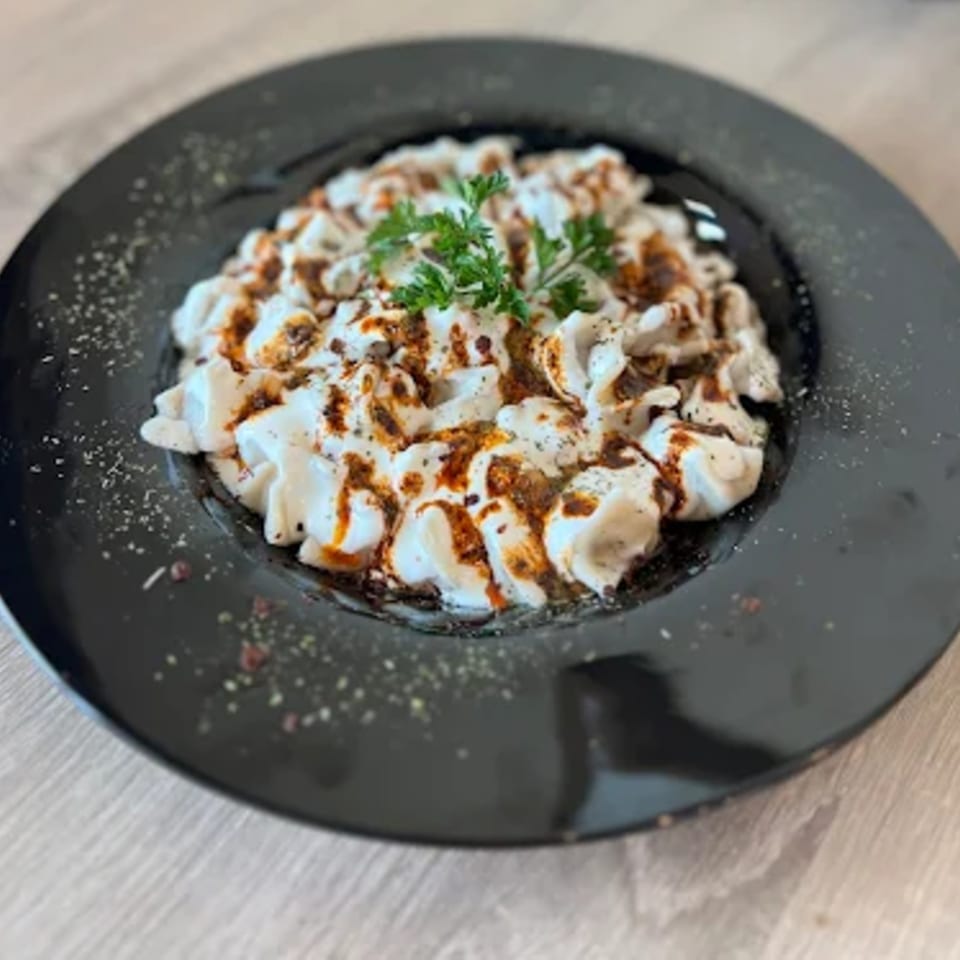 Turkish manti dumplings with yogurt, spiced oil, and fresh parsley on a black plate.