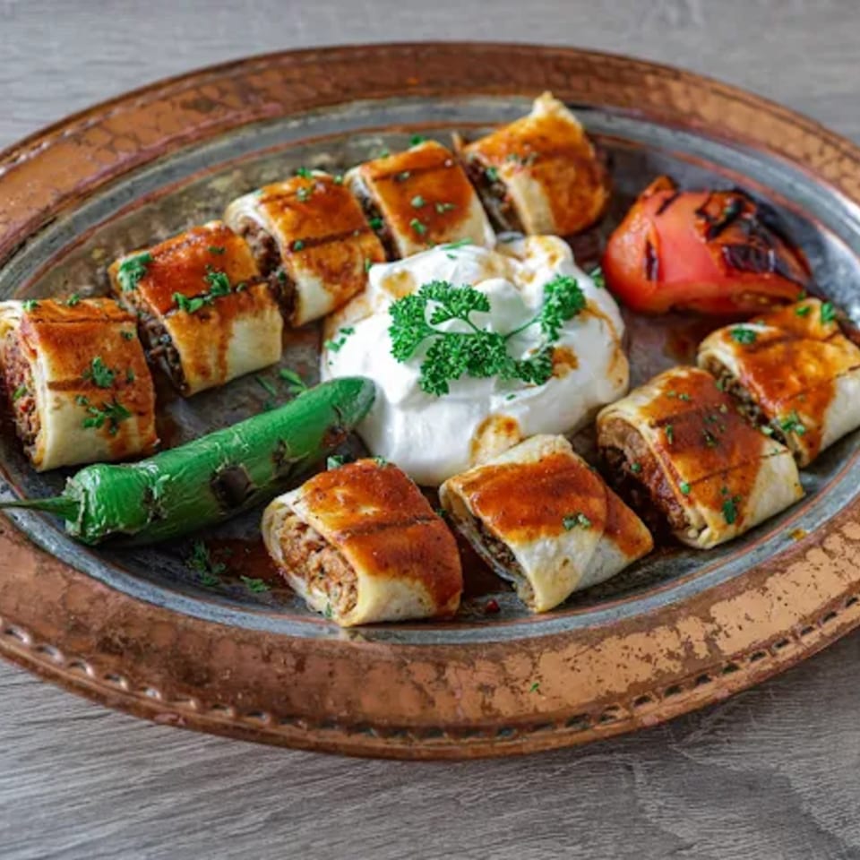 Turkish Beyti kebab rolls with yogurt, grilled tomato, and green pepper on a copper plate.