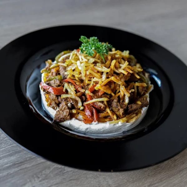 Turkish dish with seasoned meat, bell peppers, onions, and crispy fried potatoes on a bed of yogurt.